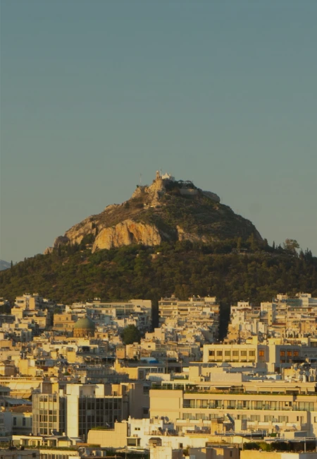 Panoramic view of Mount Lycabettus in Athens, Greece, featuring the St. George chapel and the urban skyline at sunset.