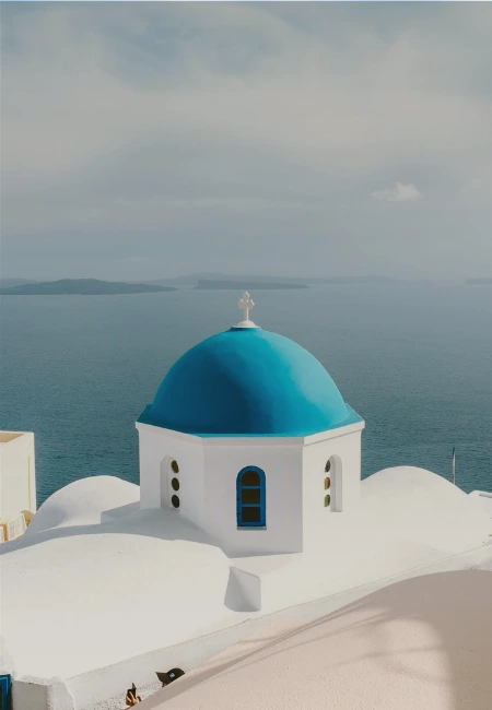 Iconic blue-domed church in Oia, Santorini, a classic example of Cycladic architecture overlooking the Aegean Sea.