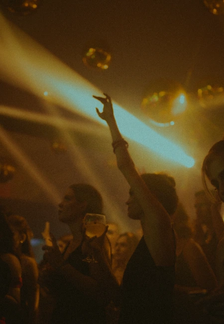 Atmosphere of a busy nightclub with golden light beams, disco balls, and people dancing.